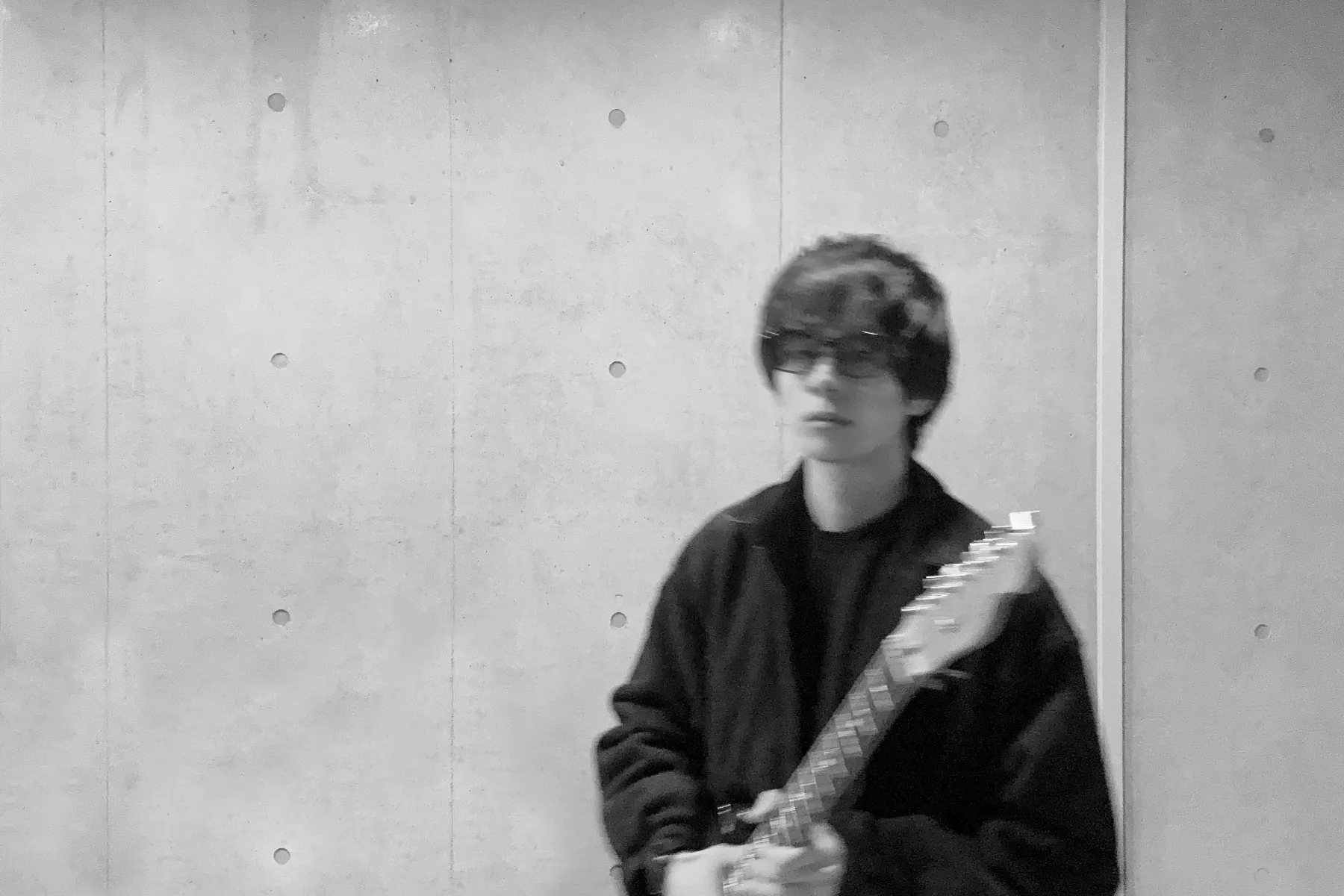 眼鏡をかけてギターを持つ人がぼやけて映されている白黒写真